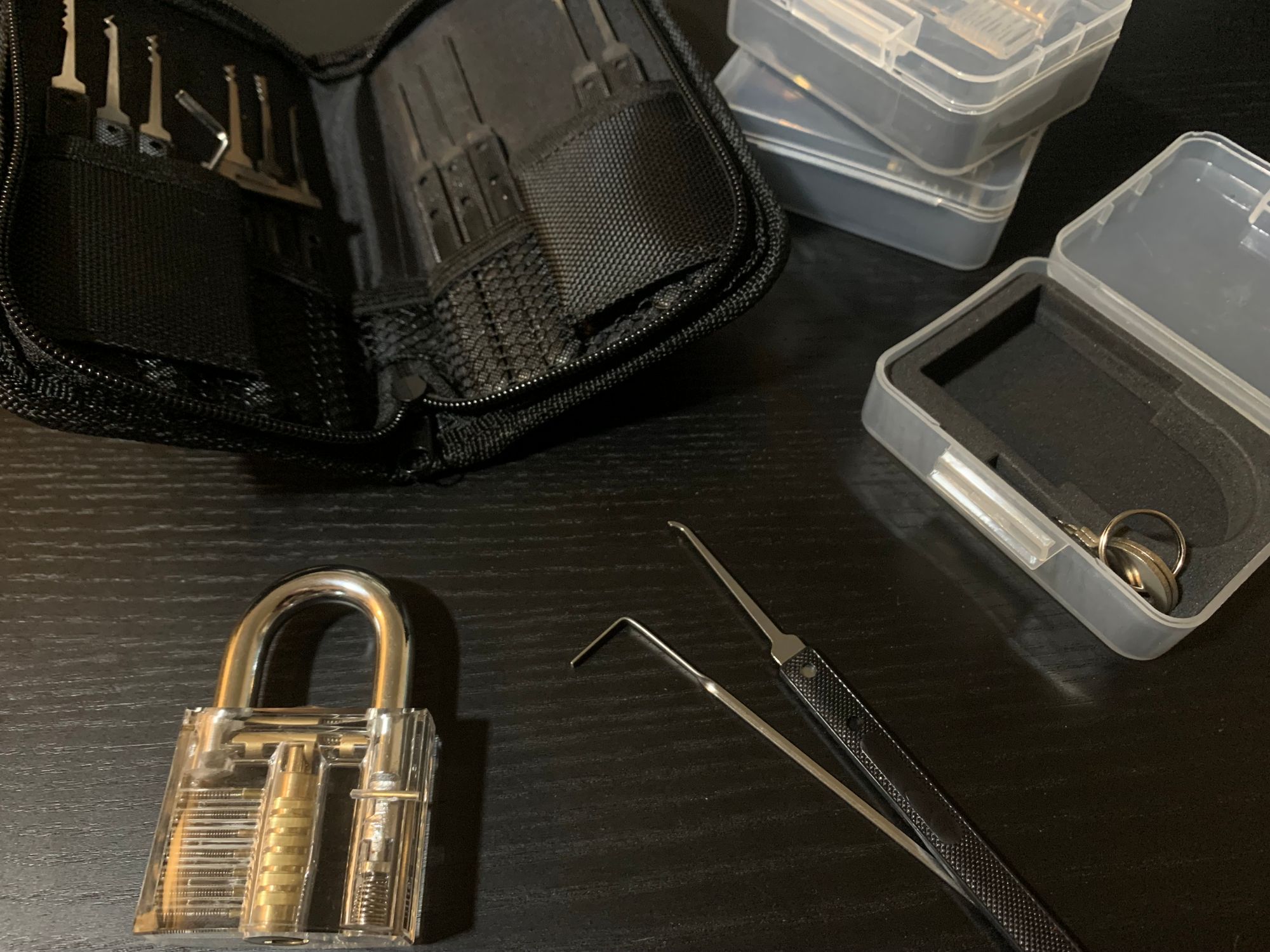 A photograph of a set of pin-tumbler lockpicks next to a transparent acrylic practice lock on a table.